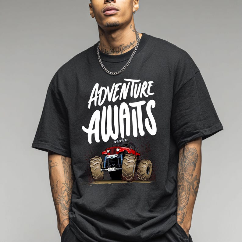 Peut inclure: T-shirt noir avec l'inscription blanche "ADVENTURE AWAITS". En dessous, un dessin d'un monster truck rouge avec de gros pneus bruns et des d&eacute;tails bleus. Le t-shirt est de style d&eacute;contract&eacute;.