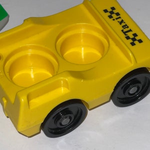 May include: Yellow plastic toy taxi with black wheels and two empty cup holders. The taxi has a black and white checkered design on the side and the word "taxi" printed on the side.