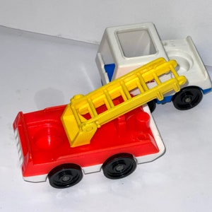 May include: A red fire truck with a yellow ladder and black wheels. The truck has a white cab and a red body. There is a white van with a blue cab and black wheels behind the fire truck.
