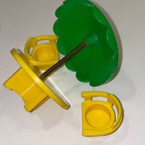 May include: A yellow plastic carousel with three seats and a green umbrella. The carousel is disassembled and the parts are spread out on a white surface.