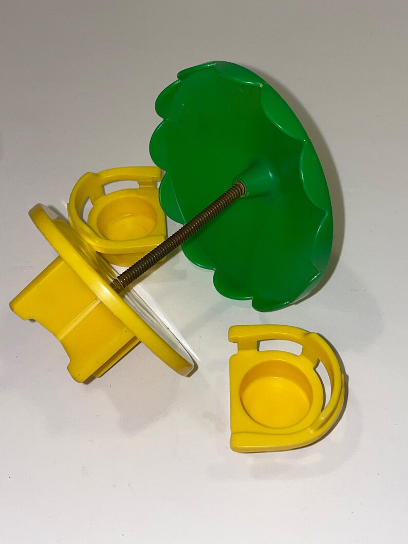 May include: A yellow plastic carousel with three seats and a green umbrella. The carousel is disassembled and the parts are spread out on a white surface.