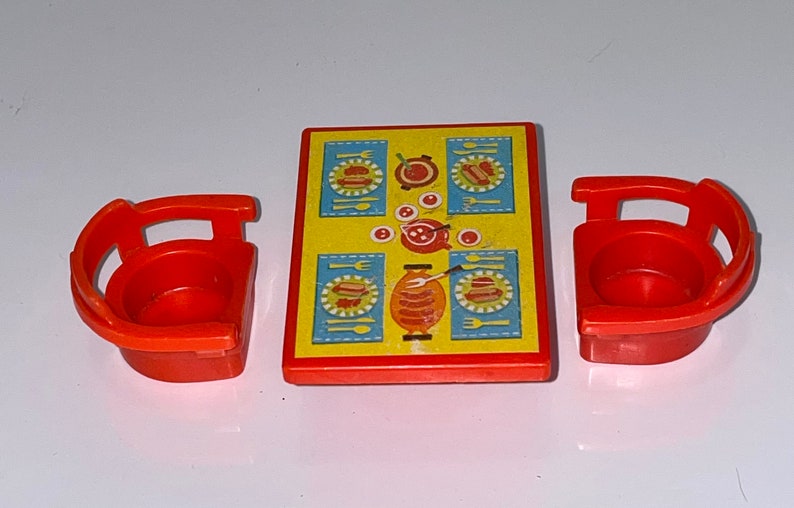 Pu&ograve; includere: Un tavolo e due sedie in plastica rossa con una tovaglia gialla e blu che presenta un hot dog e altri cibi.
