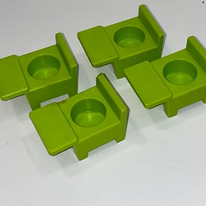 May include: Four green plastic toy chairs with attached desks. The chairs are designed for children and have a simple, rounded shape.
