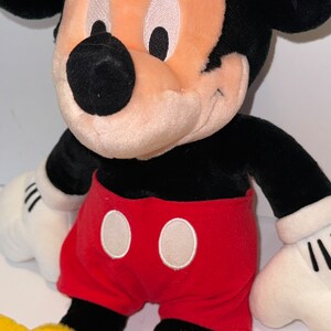 May include: A plush Mickey Mouse toy with black ears, a black nose, and white eyes. He is wearing red shorts with white circles.