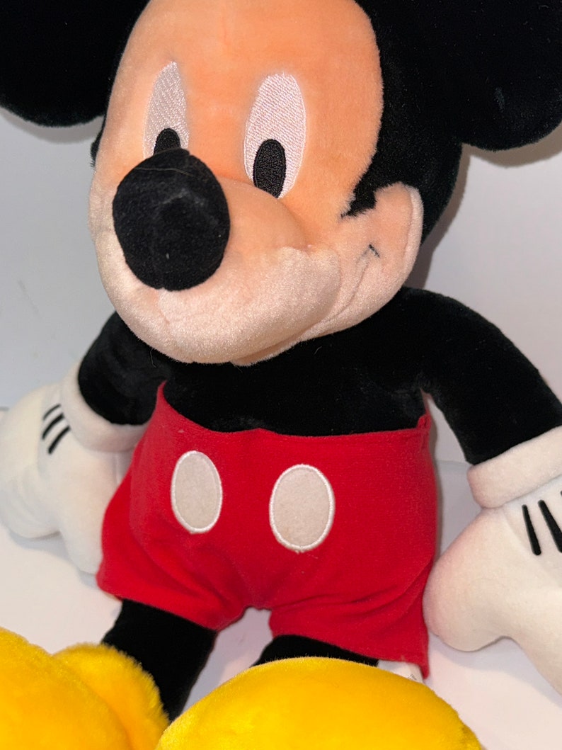 May include: A plush Mickey Mouse toy with black ears, a black nose, and white eyes. He is wearing red shorts with white circles.