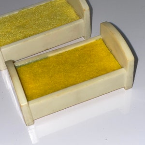May include: Two miniature white beds with yellow velvet mattresses. The beds are made of plastic and are designed for dollhouses or other miniature playsets.