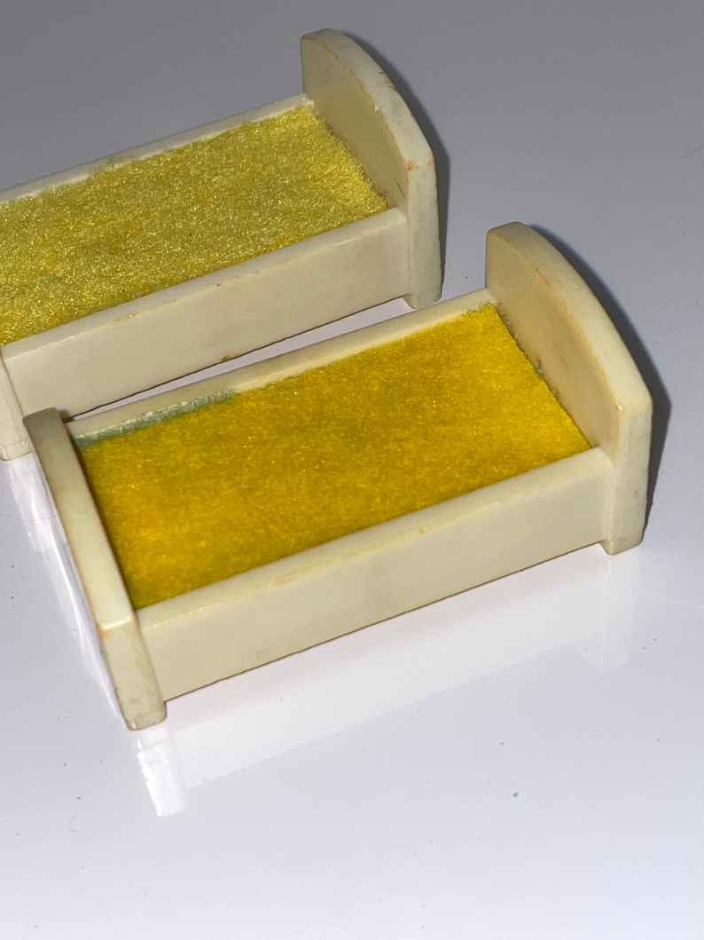 May include: Two miniature white beds with yellow velvet mattresses. The beds are made of plastic and are designed for dollhouses or other miniature playsets.