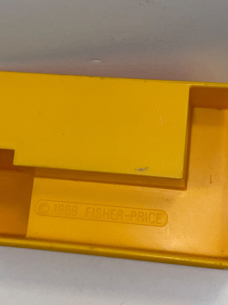K&ouml;nnte beinhalten: Gelbes Spielzeug aus Kunststoff mit einem Copyright-Symbol und dem Text "1989 FISHER-PRICE" auf der Unterseite.