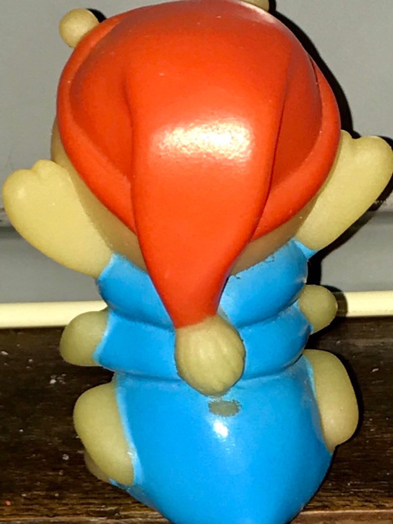 Puede incluir: Una peque&ntilde;a figura de pl&aacute;stico amarilla de una oruga que lleva un mono azul y un gorro de Pap&aacute; Noel rojo.