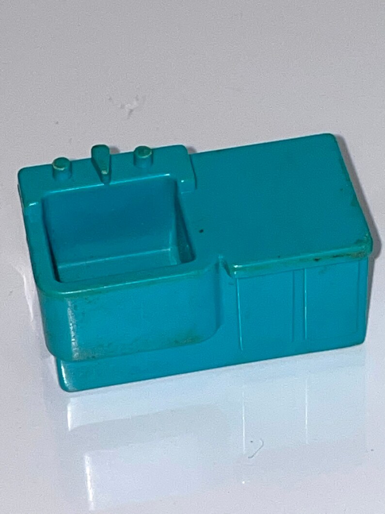 May include: A teal plastic toy kitchen sink with a single basin and two knobs. The sink is designed for play and has a simple, functional design.