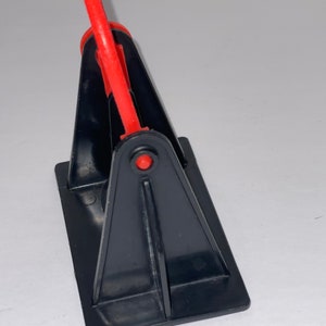 May include: A black plastic stand with a red plastic handle. The stand is designed to hold a roll of tape.