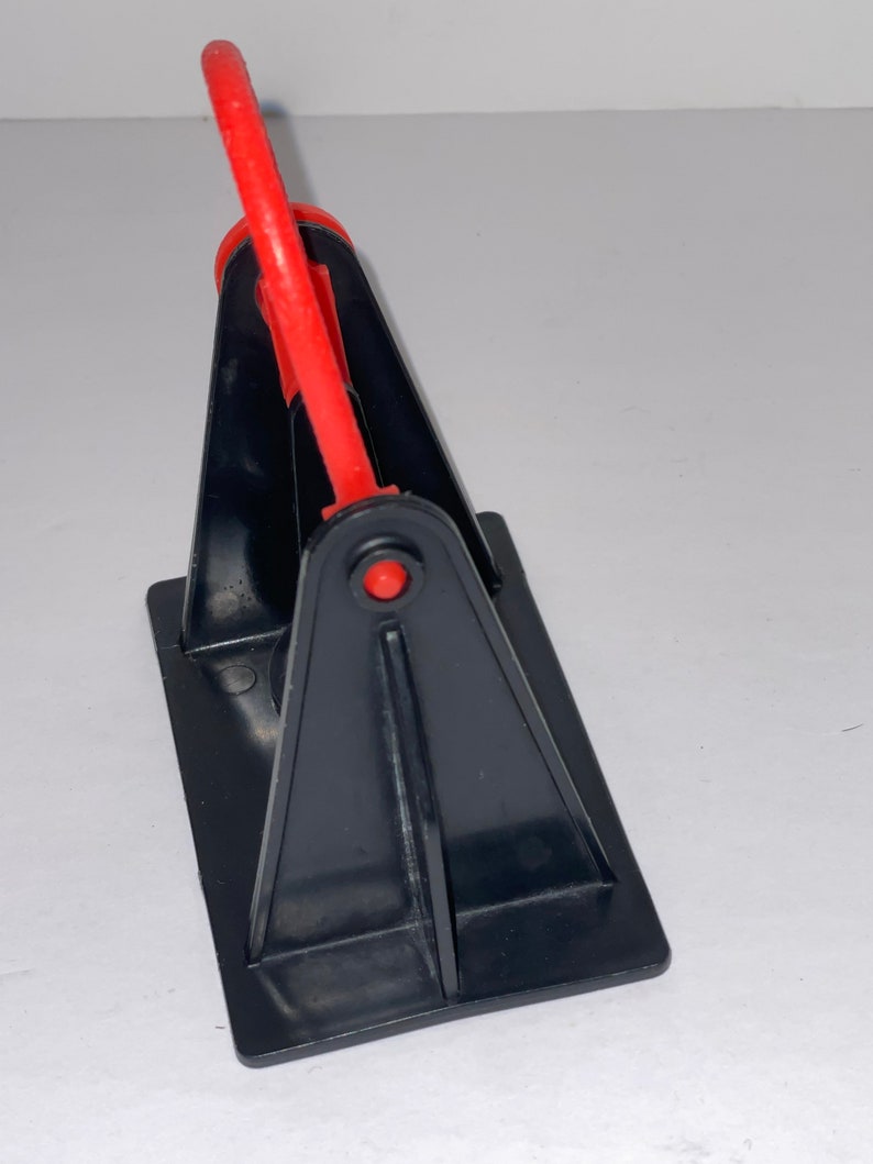 May include: A black plastic stand with a red plastic handle. The stand is designed to hold a roll of tape.