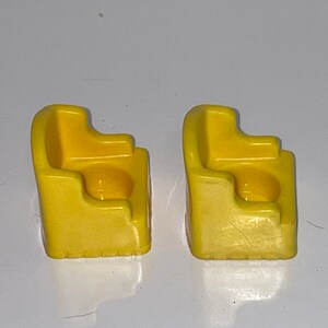 May include: Two yellow plastic chairs with a rounded back and a small seat. The chairs are designed for children and are made of a durable plastic.