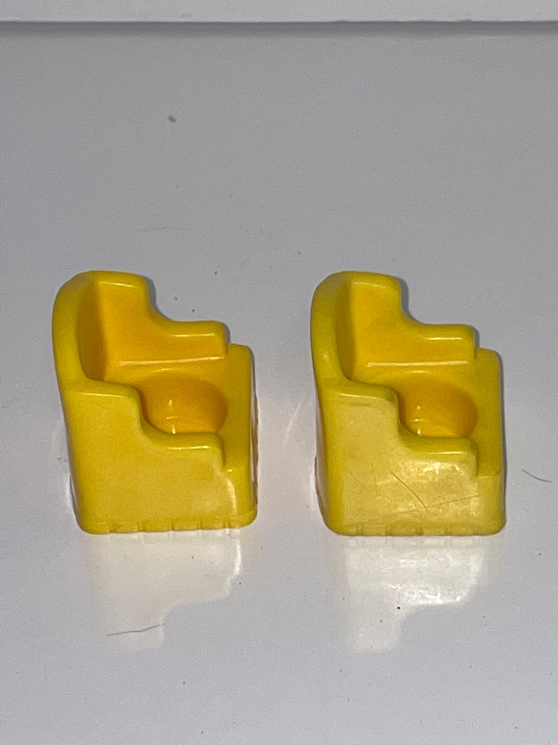 May include: Two yellow plastic chairs with a rounded back and a small seat. The chairs are designed for children and are made of a durable plastic.