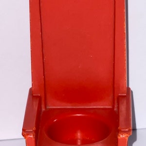 May include: A red plastic toy throne with a small, round seat. The throne has a high back and armrests.