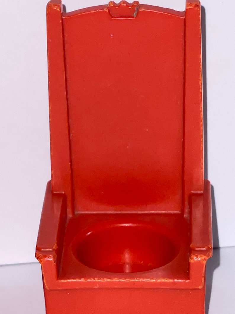 May include: A red plastic toy throne with a small, round seat. The throne has a high back and armrests.