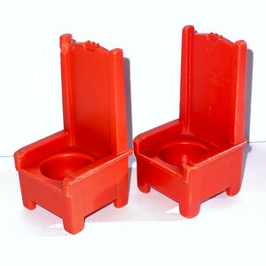 May include: Two red plastic chairs with a simple design. The chairs have a high back and a seat with a small hole in the center.