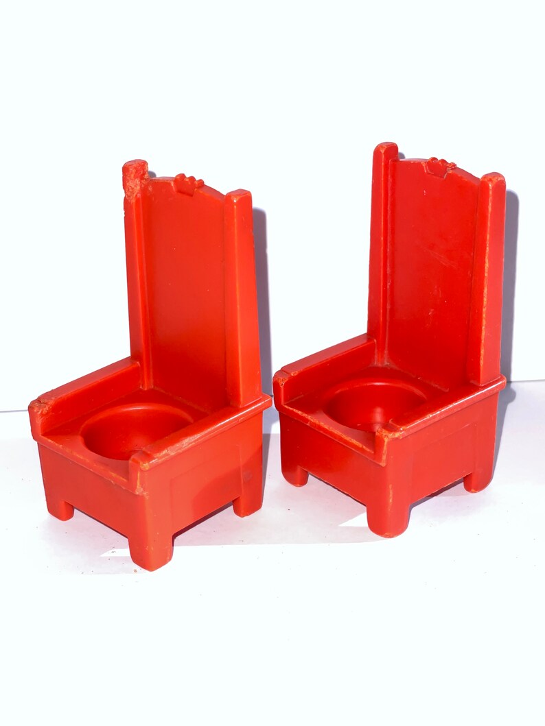 May include: Two red plastic chairs with a simple design. The chairs have a high back and a seat with a small hole in the center.