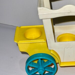 May include: A yellow and white toy wagon with a blue wheel. The wagon has two yellow cup holders and a white frame.