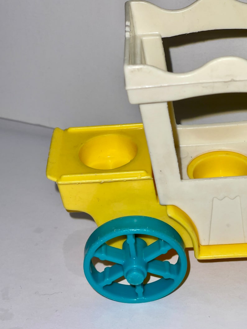 May include: A yellow and white toy wagon with a blue wheel. The wagon has two yellow cup holders and a white frame.