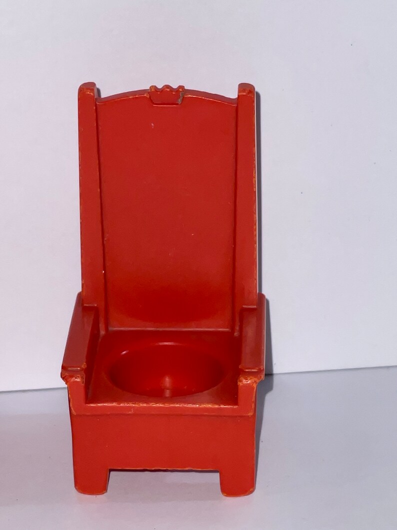 May include: A red plastic throne chair with a small seat and a crown on the back.