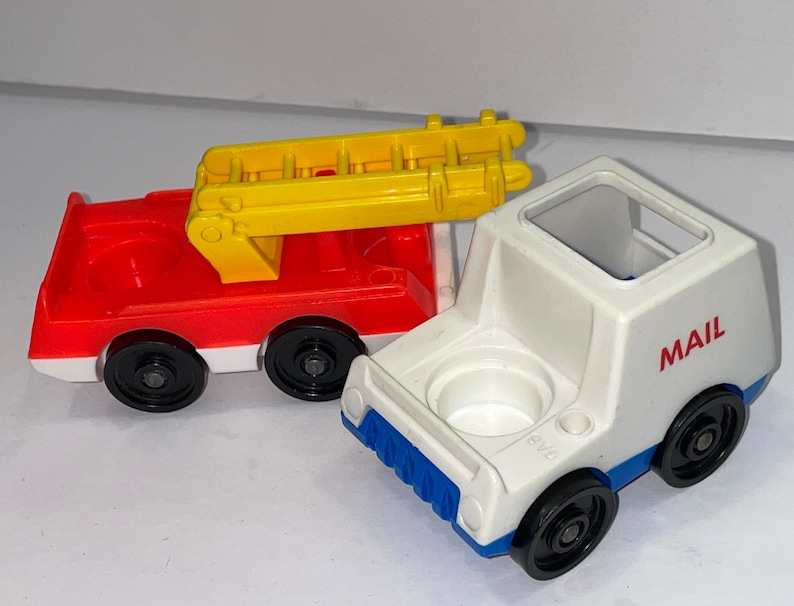 May include: Two vintage Little People toy vehicles. A red fire truck with a yellow ladder and a white mail truck with blue accents. Both trucks have black wheels and a round hole on top.