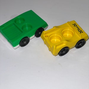 May include: Two plastic toy cars, one green and one yellow. The yellow car has "TAXI" printed on the side. Both cars have two cup holders.