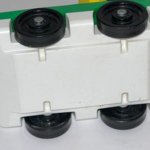 May include: A white toy truck with green and yellow accents. The truck has four black wheels and a white base.