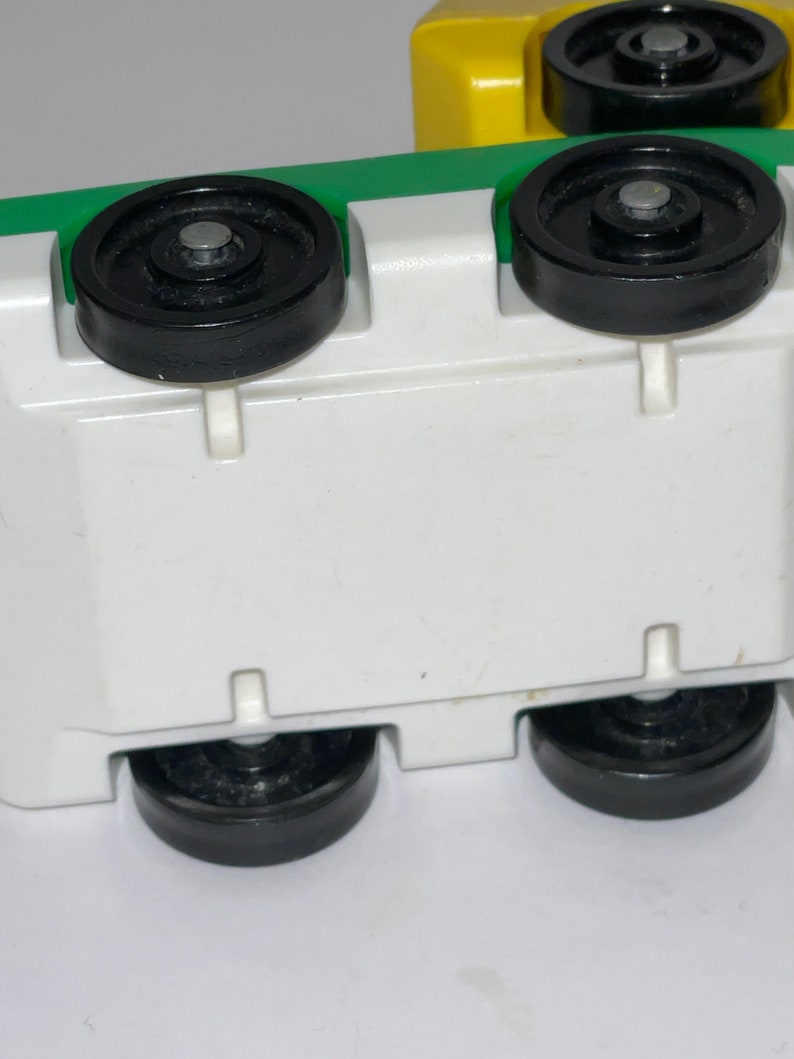 May include: A white toy truck with green and yellow accents. The truck has four black wheels and a white base.