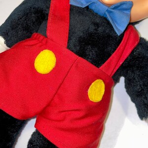 May include: A plush Mickey Mouse toy wearing red shorts with yellow buttons and a blue bow tie.