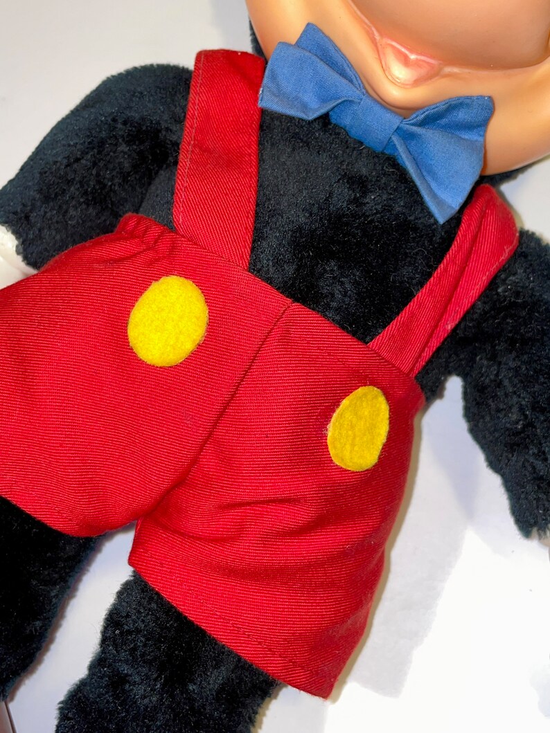May include: A plush Mickey Mouse toy wearing red shorts with yellow buttons and a blue bow tie.