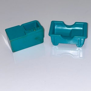 May include: Two teal blue plastic toy kitchen pieces. One is a stove with a small oven and three knobs. The other is a sink with a curved front and two small wheels.