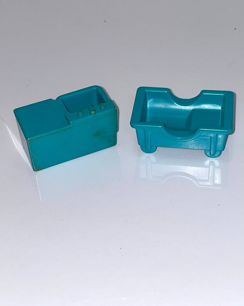 May include: Two teal blue plastic toy kitchen pieces. One is a stove with a small oven and three knobs. The other is a sink with a curved front and two small wheels.