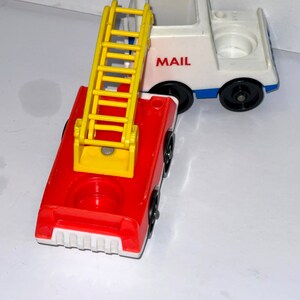 May include: A red fire truck with a yellow ladder and a white mail truck with the word "MAIL" on the side. Both trucks are made of plastic and have black wheels.