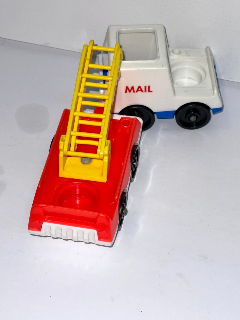 May include: A red fire truck with a yellow ladder and a white mail truck with the word "MAIL" on the side. Both trucks are made of plastic and have black wheels.
