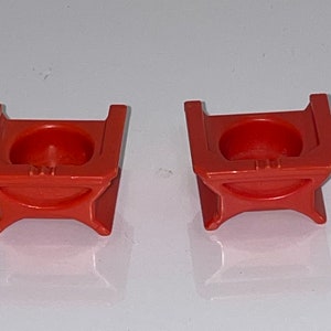 May include: Two orange plastic toy chairs with a rounded seat and a square base.