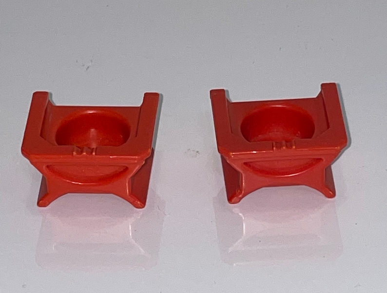 May include: Two orange plastic toy chairs with a rounded seat and a square base.