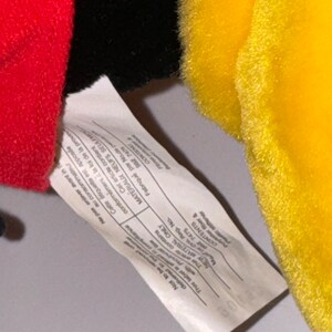 May include: White tag with black text attached to a plush toy. The tag contains information about the toy's materials and country of origin. The text reads: "Not to be delivered to the consumer. This label is affixed in compliance with the law of the province. This article contains new materials only. Polyester fiber & plastic stiffener. Contents:  Made in China."