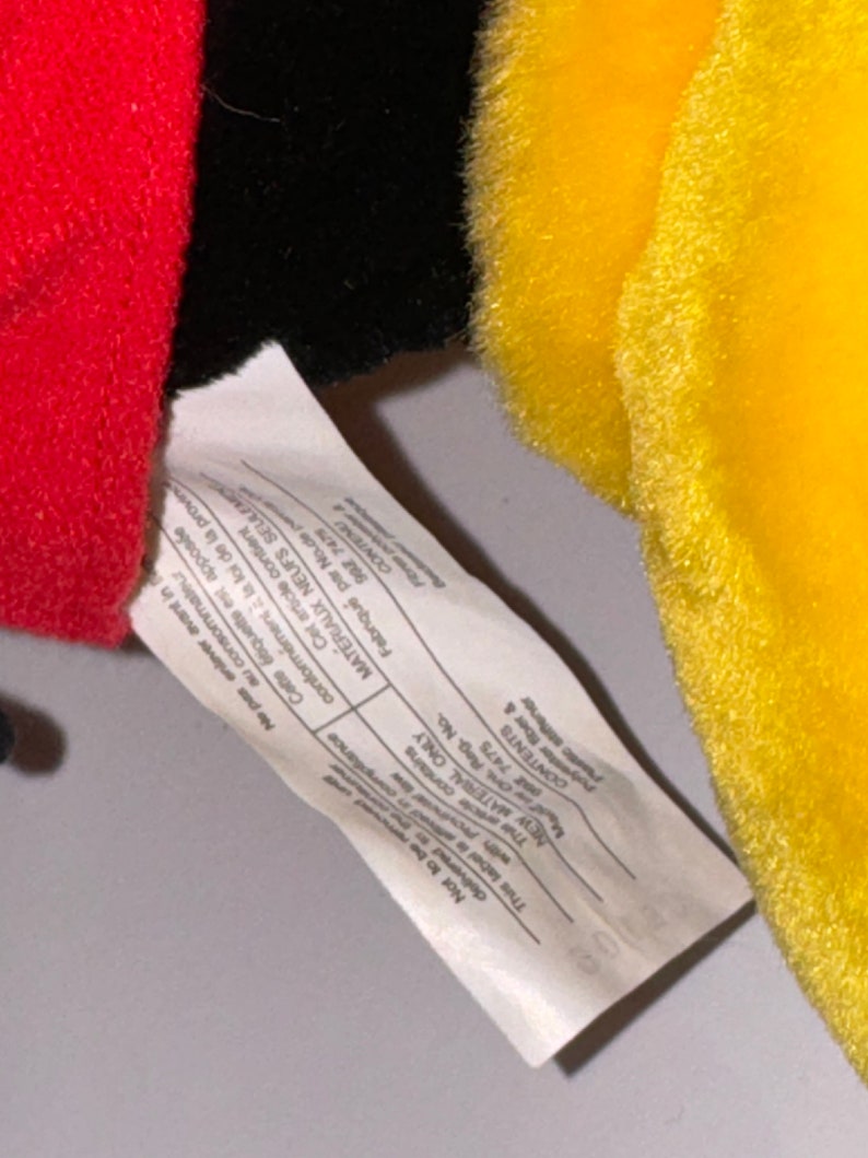 May include: White tag with black text attached to a plush toy. The tag contains information about the toy's materials and country of origin. The text reads: "Not to be delivered to the consumer. This label is affixed in compliance with the law of the province. This article contains new materials only. Polyester fiber & plastic stiffener. Contents:  Made in China."