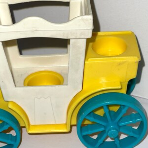 May include: A yellow and white toy carriage with blue wheels. The carriage has a white roof and two yellow seats.