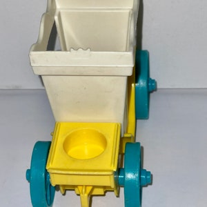 May include: A white and yellow toy wagon with blue wheels. The wagon has a square opening in the back and a round opening in the front.