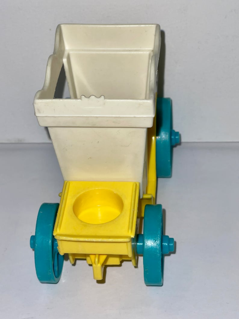 May include: A white and yellow toy wagon with blue wheels. The wagon has a square opening in the back and a round opening in the front.