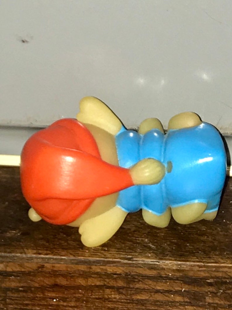 Puede incluir: Una peque&ntilde;a figura de pl&aacute;stico azul claro y naranja de un personaje durmiendo con un gorro rojo. La figura est&aacute; tumbada de lado con la cabeza apoyada en el brazo.