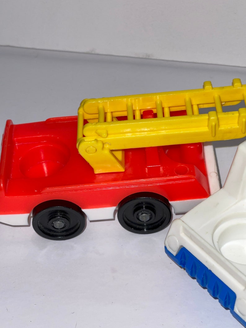 May include: A red and white toy fire truck with a yellow ladder. The truck has black wheels and a white base. The ladder is raised and has a white handle.