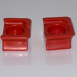 May include: Two red plastic toy building blocks with a hollow center. The blocks are square with rounded edges and have a raised lip around the top.