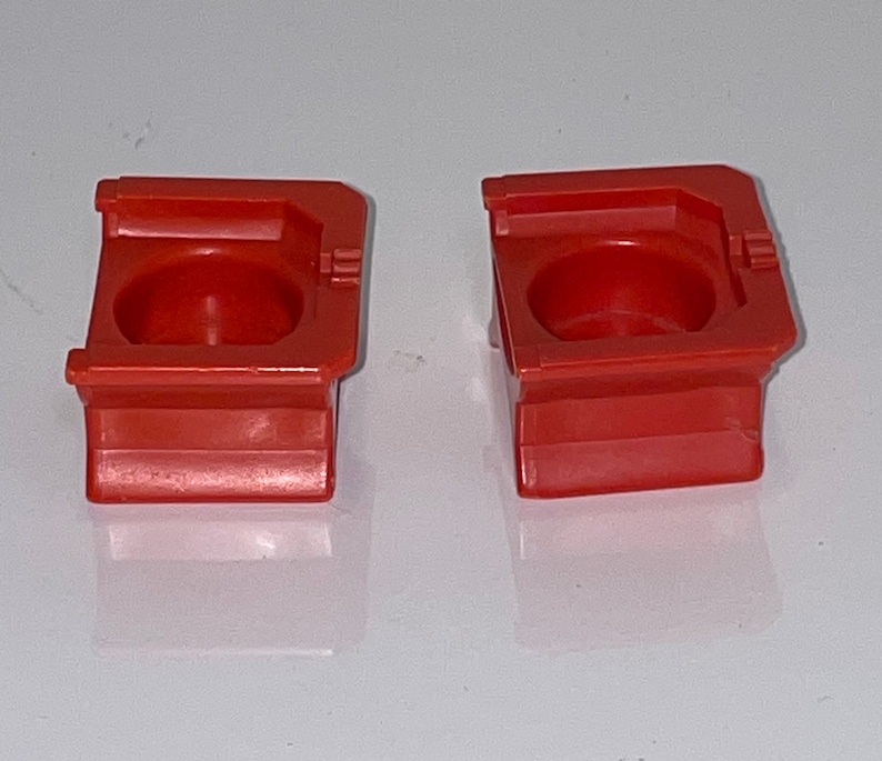 May include: Two red plastic toy building blocks with a hollow center. The blocks are square with rounded edges and have a raised lip around the top.
