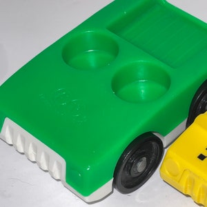 May include: Green toy truck with a white bumper and black wheels. The truck has two round indentations on the bed and a rectangular indentation with a ribbed surface. The truck is made of plastic.