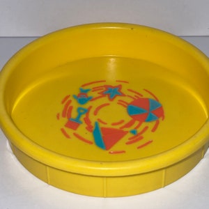 May include: A yellow plastic kiddie pool with a beach scene design. The design includes a blue and red beach ball, a blue fish, a blue and orange shovel, and a blue star.