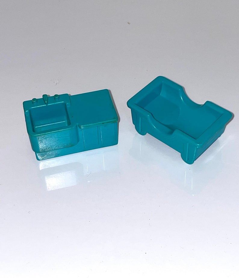 May include: Two teal plastic toy furniture pieces. One is a sink with a faucet and the other is a bed.