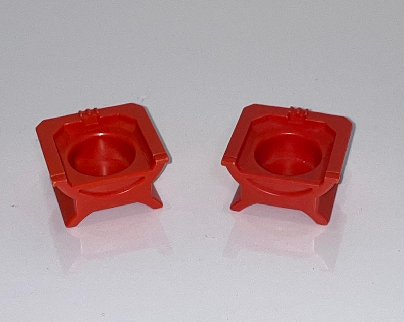 May include: Two red plastic throne chairs with a small, round seat and a decorative design on the top. The chairs are made of a smooth, glossy plastic.